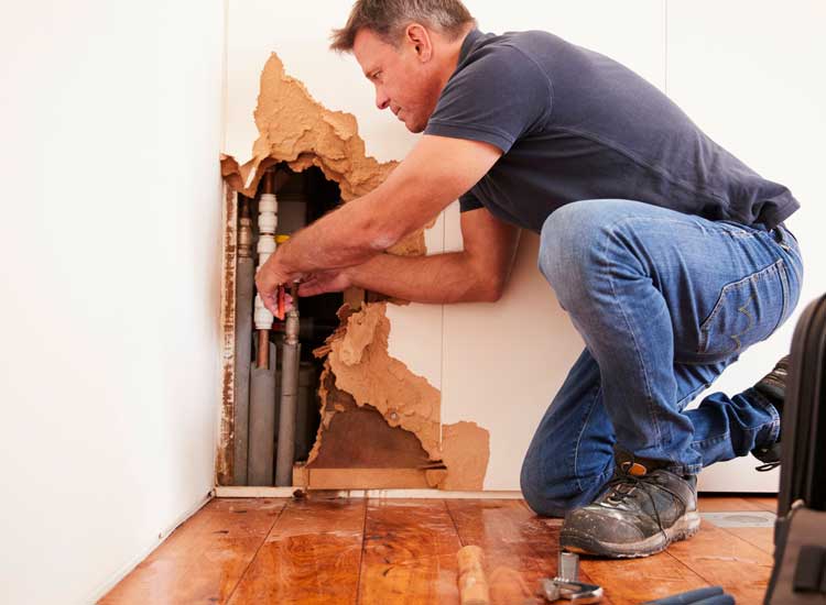 Man performing water damage remediation on a pipe in a wall with Stallion Restoration