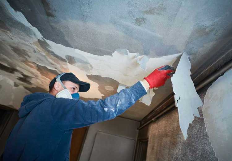 man performing Water Remediation Services on a damaged ceiling with Stallion Restoration